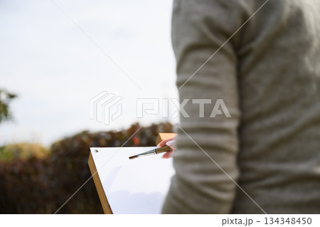 Close-up of artist painting on blank canvas outdoors. Close-up of artist painting on blank canvas outdoors. 134348450