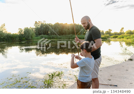 Father and son fishing together at river during sunset 134348490