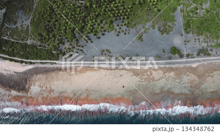 French Polynesia, Rangiroa island: Aerial view tranquil beachfront colorful waves meet a sandy shore, surrounded by greenery. The road runs alongside the coastline, highlighting scenic beauty. 134348762