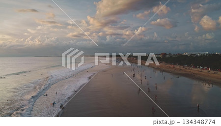 Dreamland Beach in Bali, Indonesia, showcases a stunning sunset scene with tourists along the shoreline, gentle waves, and a peaceful, cloudy sky 134348774