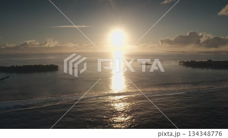 Golden sunlight gracefully illuminates the ocean surface, creating shimmering reflections. Distant islands silhouette against the horizon, casting serene vibes at dusk. 134348776