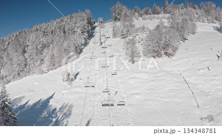 Chairlift ascending a snowy mountain slope on bright, sunny winter day, stunning views of snow covered trees and ski slopes stretching below. Bukovel ski resort. Winter wild nature travel background 134348781