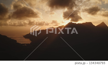 Moorea island landscape presenting a vibrant sunset over a mountain range, creating dramatic silhouettes and illuminating the tropical bay below with warm golden light through atmospheric clouds Moorea island landscape presenting a vibrant sunset over a mountain range, creating dramatic silhouettes and illuminating the tropical bay below with warm golden light through atmospheric clouds 134348793