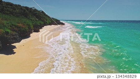 Breathtaking aerial view capturing turquoise ocean waves gently crashing on a pristine sandy beach, surrounded by lush green vegetation on Sumba Island, Indonesia 134348829