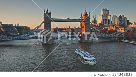 Aerial view of Tower Bridge, one of London's most famous landmarks, City Hall, River Thames and skyscrapers of City of London in background at sunset. Tourist excursion boat. Drone flight 134348832
