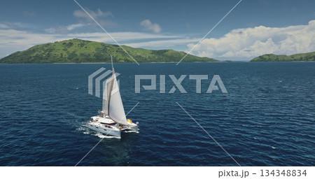Fiji, Kuata island: aerial view people relax on luxury catamaran sailing blue ocean near tropical island with green hills. Remote wild nature paradise, exotic summer travel. Drone flight 134348834
