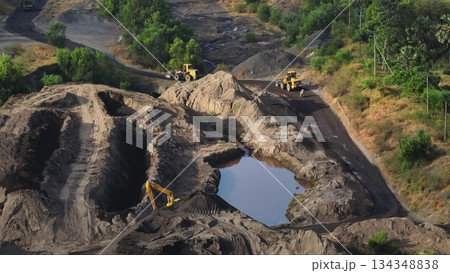 Quarry operations with excavators, bulldozers and wheel loaders moving sand and soil piles, shaping terrain around water-filled pit in active open-pit mining site. Industrial concept. Aerial panorama Quarry operations with excavators, bulldozers and wheel loaders moving sand and soil piles, shaping terrain around water-filled pit in active open-pit mining site. Industrial concept. Aerial panorama 134348838