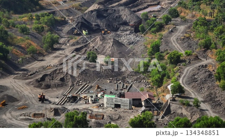 Large scale open pit mining operation showing excavators, dump trucks, and various industrial equipment actively extracting coal from the landscape, forming vast piles of raw material 134348851