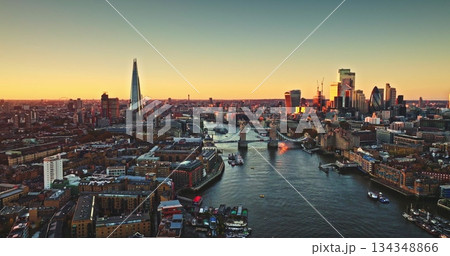 England, aerial London skyline at sunset with iconic landmarks Tower Bridge, The Shard skyscraper, and illuminated buildings of Canary Wharf on River Thames. Modern cityscape under bright evening sky England, aerial London skyline at sunset with iconic landmarks Tower Bridge, The Shard skyscraper, and illuminated buildings of Canary Wharf on River Thames. Modern cityscape under bright evening sky 134348866