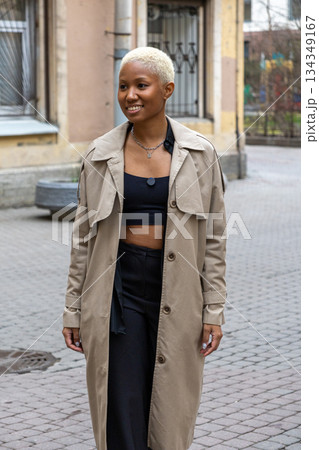 African American woman with short blond hair, wearing a beige coat, smiles.  134349167