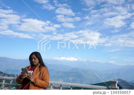 Woman Using Smartphone with Panoramic View of Snowy Himalayan Mountains in Background Woman Using Smartphone with Panoramic View of Snowy Himalayan Mountains in Background 134350057