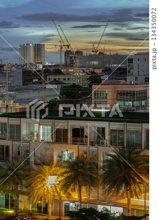 The cityscape sunset features multi-story buildings and construction cranes silhouetted against a bright horizon 134350072