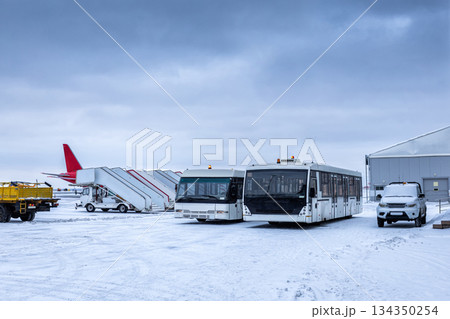 Two airport shuttle buses, empty passenger boarding stairs and other equipment on the winter airport Two airport shuttle buses, empty passenger boarding stairs and other equipment on the winter airport 134350254