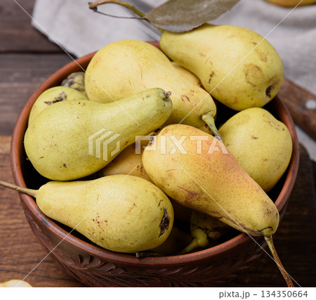 Ripe yellow green pears in a brown ceramic bowl on a wooden table 134350664