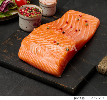 A close-up of a piece of fresh salmon on a black wooden board. A close-up of a piece of fresh salmon on a black wooden board. 134351234