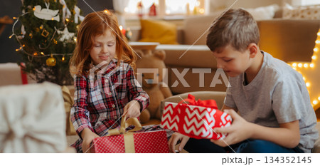 Siblings opening christmas presents in pajamas. Siblings opening christmas presents in pajamas. 134352145