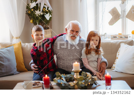 Kids spending Christmas time with senior grandfather indoors at home. Kids spending Christmas time with senior grandfather indoors at home. 134352162