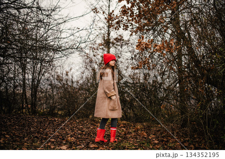 Young girl standing in nature wearing red hat. 134352195
