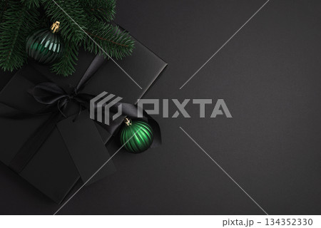 Black Christmas Gift Box with Satin Ribbon and Green Ornaments on Dark Holiday Background Black Christmas Gift Box with Satin Ribbon and Green Ornaments on Dark Holiday Background 134352330