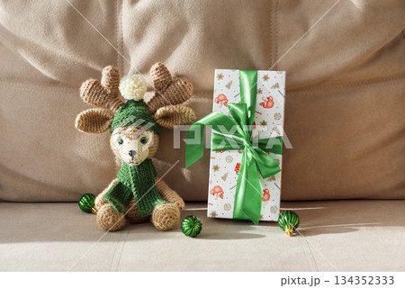 Crocheted Reindeer with Christmas Gift Box and Ornaments on Cozy Holiday Background 134352333