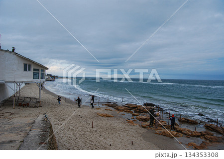 Overcast day at a rocky beach with ocean waves and coastal building. Overcast beach scene featuring a rocky shoreline and ocean waves in Odessa. Overcast day at a rocky beach with ocean waves and coastal building. Overcast beach scene featuring a rocky shoreline and ocean waves in Odessa. 134353308