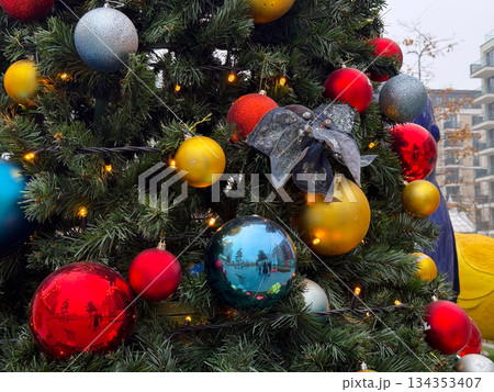 Decorated Christmas tree with colorful baubles and lights in urban park. Holiday ornament details, winter celebration, and festive outdoor decor Decorated Christmas tree with colorful baubles and lights in urban park. Holiday ornament details, winter celebration, and festive outdoor decor 134353407
