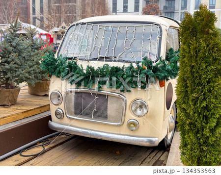 Vintage van decorated with Christmas garland and lights at winter market. Festive urban installation, seasonal decor and holiday atmosphere 134353563