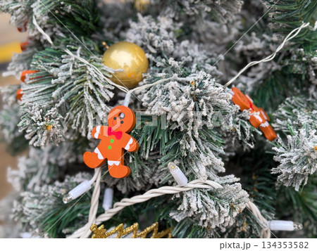 Gingerbread figure ornament on snow covered Christmas tree. Festive winter decor, playful detail and seasonal holiday atmosphere 134353582