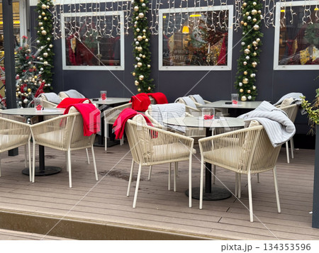 Outdoor cafe terrace decorated for Christmas with blankets and lights. Winter leisure space, seasonal hospitality and festive urban atmosphere Outdoor cafe terrace decorated for Christmas with blankets and lights. Winter leisure space, seasonal hospitality and festive urban atmosphere 134353596