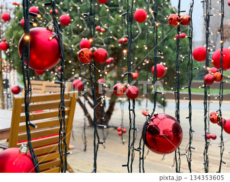 Red Christmas baubles hanging on string lights in outdoor setting. Festive urban decor, winter atmosphere and seasonal holiday illumination Red Christmas baubles hanging on string lights in outdoor setting. Festive urban decor, winter atmosphere and seasonal holiday illumination 134353605