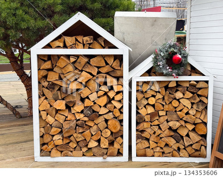 Firewood neatly stacked in white wooden storage houses in Christmas time. Winter preparation, rustic decor and cozy outdoor atmosphere Firewood neatly stacked in white wooden storage houses in Christmas time. Winter preparation, rustic decor and cozy outdoor atmosphere 134353606