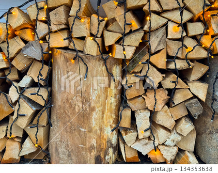 Stacked firewood decorated with warm string lights for Christmas season. Rustic winter background, cozy holiday atmosphere and traditional outdoor styling. Stacked firewood decorated with warm string lights for Christmas season. Rustic winter background, cozy holiday atmosphere and traditional outdoor styling. 134353638