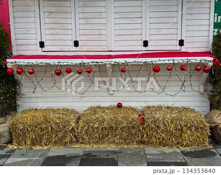 Empty Christmas market stall decorated with red ornaments, string lights and hay bales. Seasonal winter setup, festive anticipation and rustic holiday atmosphere. 134353640