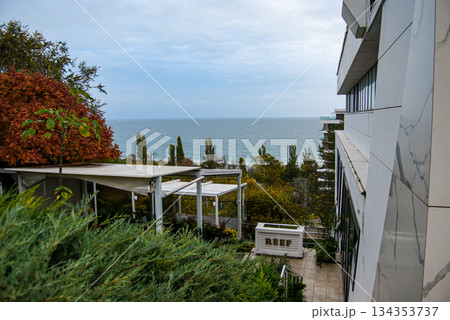 Coastal resort view with autumn trees and ocean horizon. Modern coastal resort with a sleek building featuring a marble facade on the right. 134353737