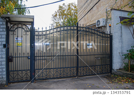 Ornate wrought iron gate entrance to a property. Ornate wrought iron gate features intricate scroll patterns and spearhead finials.  134353791