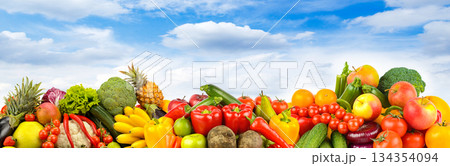 Assorted fresh fruits and vegetables arranged outdoors under blue sky with scattered clouds 134354094