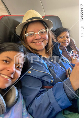 Three women are sitting on a plane, smiling and posing for a picture 134354417