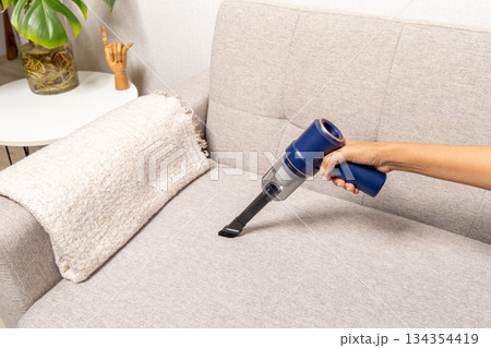 A person is vacuuming a couch with a blue vacuum cleaner 134354419