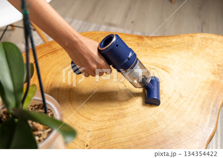 A person is cleaning a wooden table with a vacuum cleaner A person is cleaning a wooden table with a vacuum cleaner 134354422