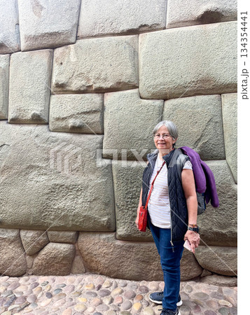 A woman stands in front of a stone of the 12 angles, wearing a purple backpack. Cusco, Peru 134354441