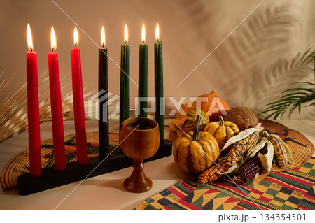 Kwanzaa Celebration Setting. Warm Kwanzaa scene with lit candles, harvest vegetables, and a wooden chalice Kwanzaa Celebration Setting. Warm Kwanzaa scene with lit candles, harvest vegetables, and a wooden chalice 134354501