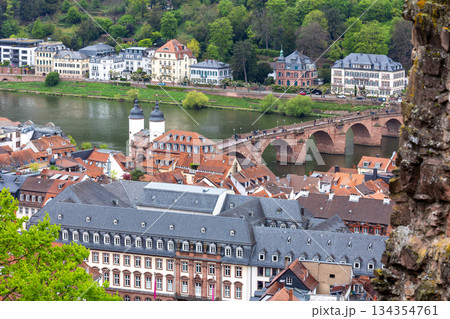 Panoramic view Heidelberg oldtown with historic stone bridge over Neckar river and red tiled rooftops. Scenic European cityscape shows heritage architecture, green hillside and urban river landscape. 134354761