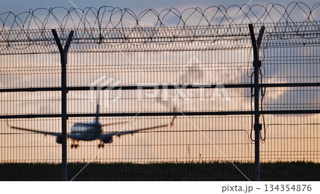 Airplane landing behind airport fence at sunset representing travel restrictions Airplane landing behind airport fence at sunset representing travel restrictions 134354876