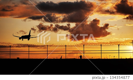Airplane landing at sunset over airport perimeter fence Airplane landing at sunset over airport perimeter fence 134354877
