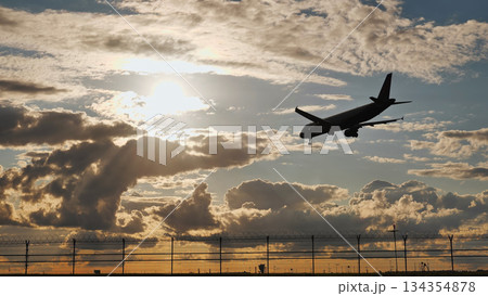 Passenger airplane landing at sunset over airport fence 134354878