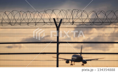 Airplane landing behind airport fence with barbed wire at sunset 134354888