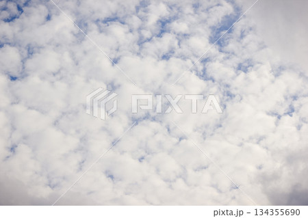 White, fluffy altocumulus clouds covering a large part of a bright blue sky on a sunny day 134355690