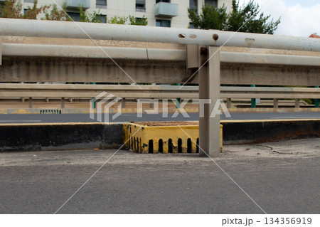 Concrete divider on a busy roadway with a drainage grate in an urban setting Concrete divider on a busy roadway with a drainage grate in an urban setting 134356919