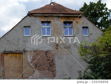 Old building with peeling paint and exposed bricks under a cloudy sky 134356958