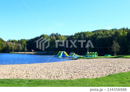 Colorful water park features and sandy beach beside a serene lake surrounded Colorful water park features and sandy beach beside a serene lake surrounded 134356986